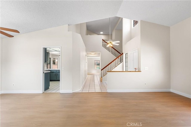 unfurnished living room with a ceiling fan, light wood-style floors, a textured ceiling, stairs, and baseboards