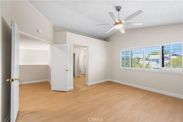 unfurnished bedroom with lofted ceiling, light wood-type flooring, a textured ceiling, baseboards, and a ceiling fan
