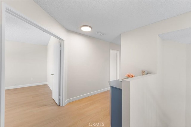 hall featuring light wood-style floors, a textured ceiling, and baseboards