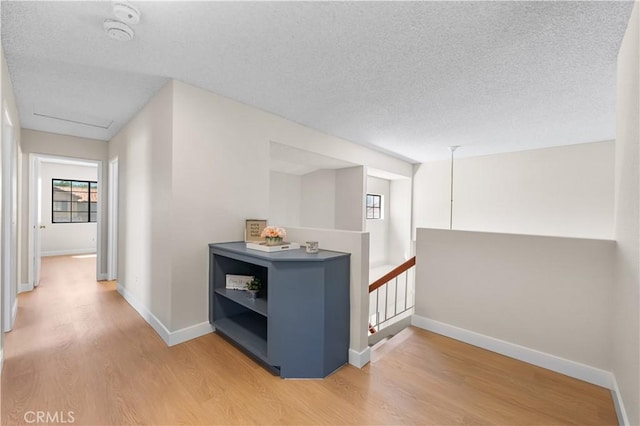 hallway with light wood finished floors, an upstairs landing, a textured ceiling, and baseboards