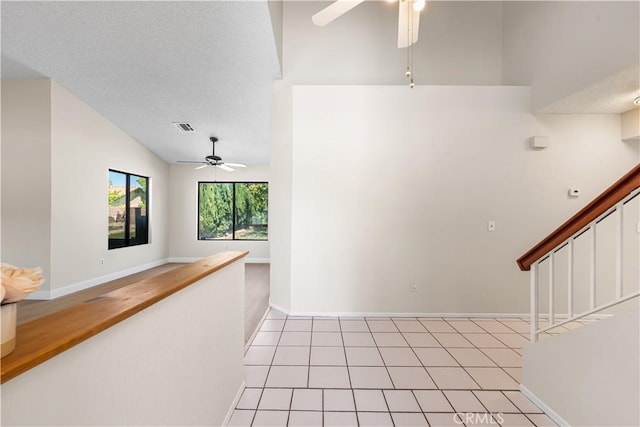corridor with lofted ceiling, baseboards, stairs, a textured ceiling, and light tile patterned floors