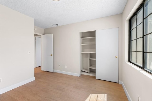 unfurnished bedroom featuring multiple windows, wood finished floors, baseboards, a textured ceiling, and a closet