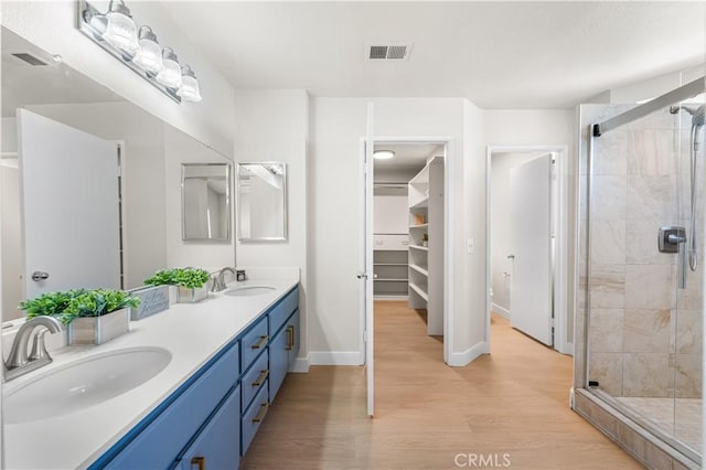 bathroom featuring a stall shower, wood finished floors, double vanity, and baseboards