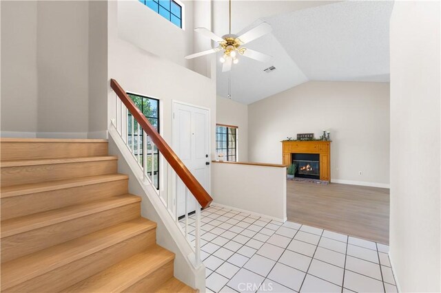 staircase with healthy amount of natural light, a ceiling fan, tile patterned flooring, a glass covered fireplace, and lofted ceiling