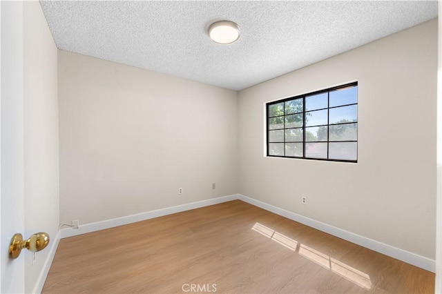 empty room with light wood-style floors, baseboards, and a textured ceiling
