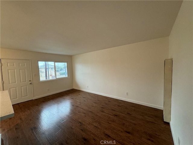 spare room featuring dark wood-style flooring and baseboards