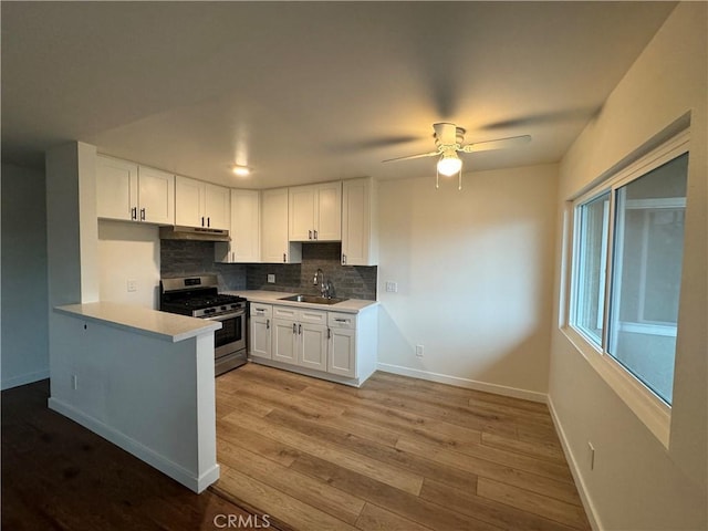 kitchen with gas range, a sink, under cabinet range hood, tasteful backsplash, and white cabinetry