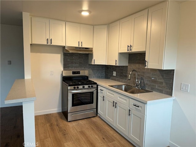 kitchen featuring gas stove, a sink, under cabinet range hood, and white cabinets
