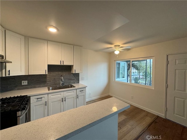 kitchen with a sink, stainless steel gas range oven, baseboards, backsplash, and white cabinets