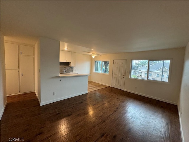 unfurnished living room featuring dark wood-type flooring, baseboards, a sink, and a ceiling fan