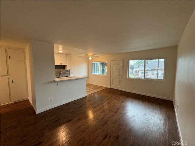 unfurnished living room with dark wood-style floors, baseboards, ceiling fan, and a sink