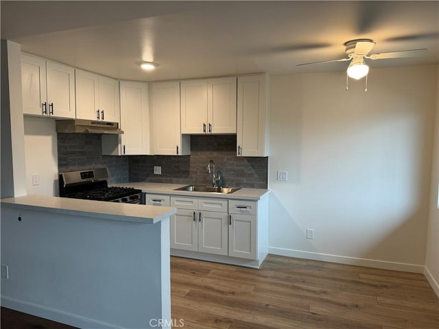 kitchen featuring gas range, a sink, white cabinets, baseboards, and ceiling fan