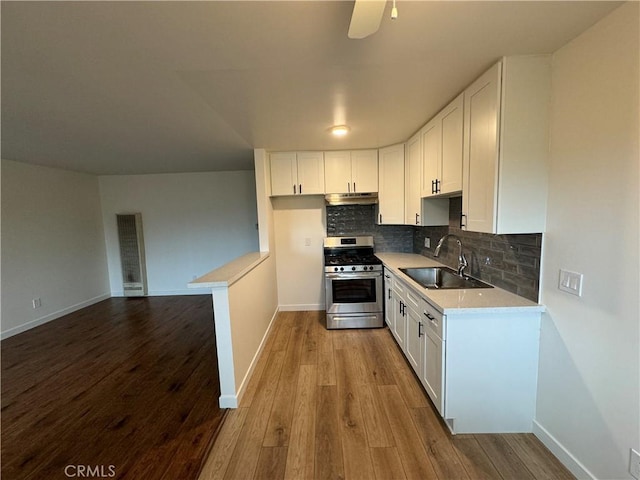 kitchen featuring stainless steel gas range oven, a sink, under cabinet range hood, light countertops, and wood finished floors