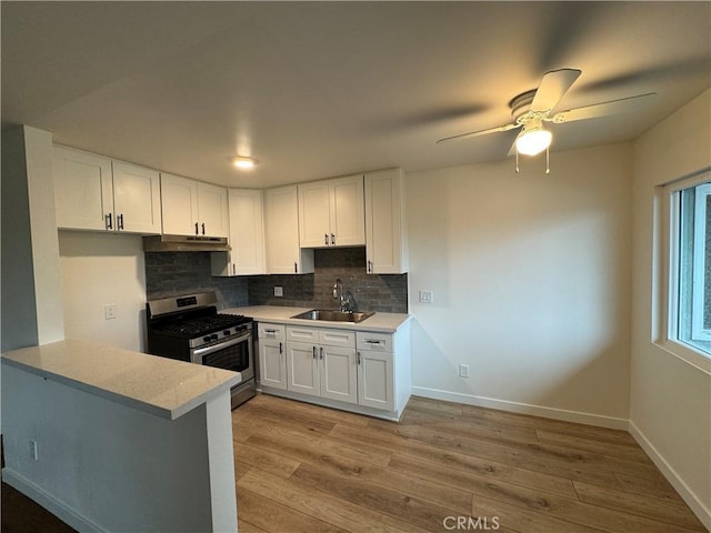 kitchen featuring stainless steel gas stove, a sink, under cabinet range hood, white cabinetry, and backsplash
