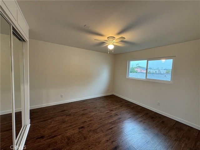 unfurnished bedroom with dark wood-style floors, baseboards, a closet, and ceiling fan
