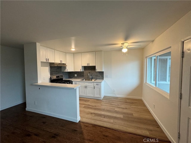 kitchen with a sink, gas stove, white cabinets, light countertops, and tasteful backsplash