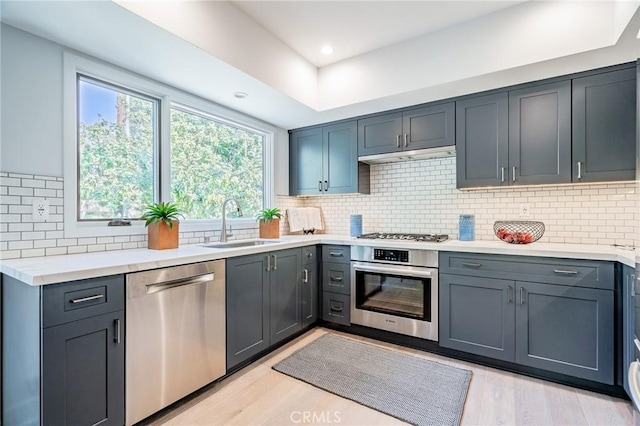 kitchen featuring appliances with stainless steel finishes, a sink, light wood-style flooring, light countertops, and decorative backsplash