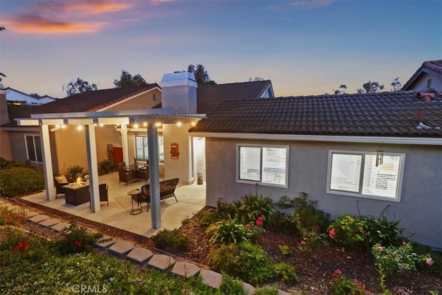 24082 Calendula, Mission Viejo, CA 92692 - back of house at dusk featuring a patio, stucco siding, a chimney, and a tiled roof