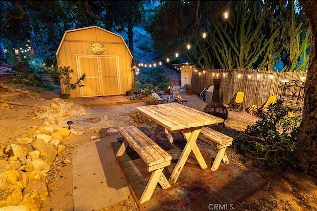 patio at twilight with a shed, an outdoor structure, outdoor dining space, and fence