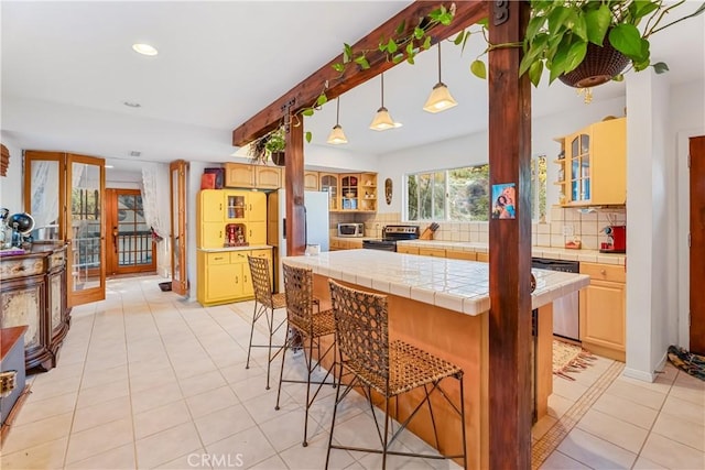 kitchen with stainless steel appliances, tile countertops, decorative backsplash, a kitchen breakfast bar, and glass insert cabinets