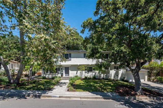 view of property hidden behind natural elements featuring a front yard, stucco siding, and concrete driveway