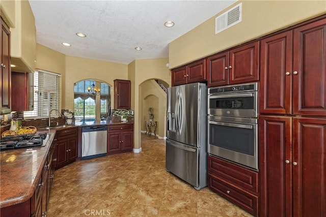 44886 Camino Veste, Temecula, CA 92592 - kitchen with stainless steel appliances, reddish brown cabinets, arched walkways, a sink, and a textured ceiling