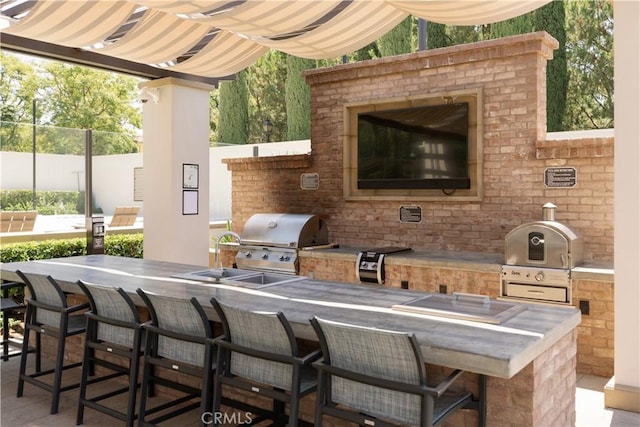 view of patio / terrace with exterior kitchen, a grill, fence, and a sink