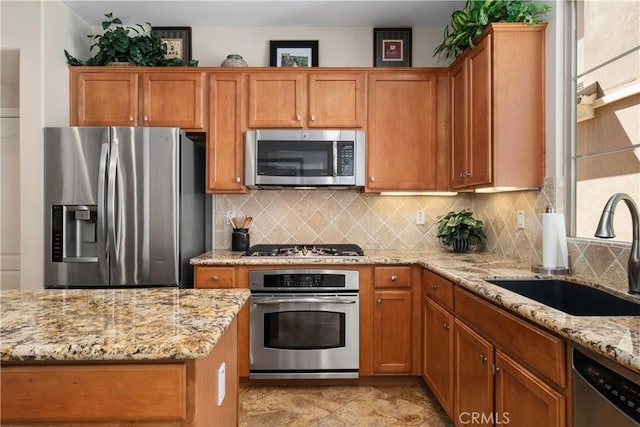 kitchen featuring stainless steel appliances, a sink, decorative backsplash, light stone counters, and brown cabinetry