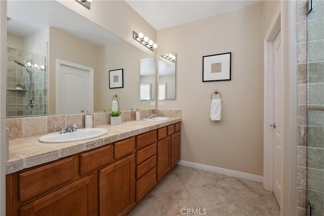 bathroom with tile patterned floors, tiled shower, double vanity, and baseboards