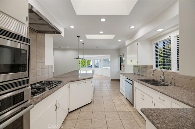 kitchen featuring appliances with stainless steel finishes, a sink, backsplash, a skylight, and wall chimney range hood