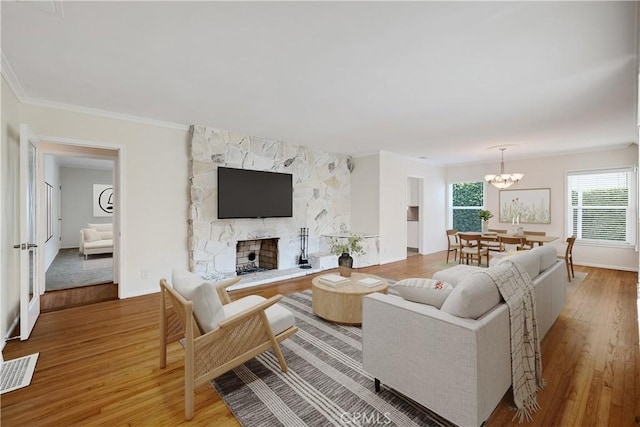 living area with light wood-type flooring, a chandelier, a fireplace, ornamental molding, and baseboards