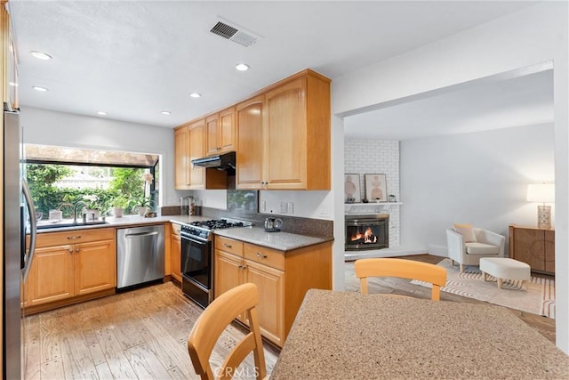 15 Firestone Unit 4, Irvine, CA 92614 - kitchen with stainless steel appliances, light wood-style floors, a sink, a fireplace, and under cabinet range hood