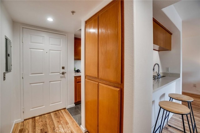 hallway with light wood finished floors, electric panel, recessed lighting, and a sink