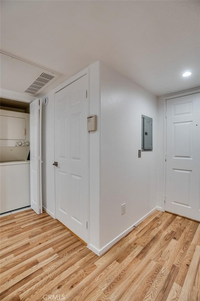 hallway featuring estacked washer and dryer, light wood-style floors, electric panel, baseboards, and recessed lighting