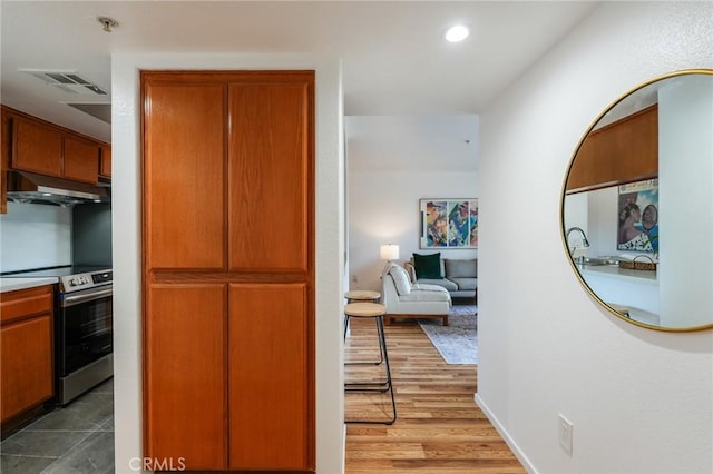 kitchen featuring under cabinet range hood, electric range, recessed lighting, wood finished floors, and brown cabinetry