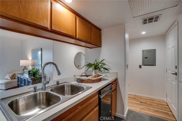 kitchen with dishwashing machine, brown cabinetry, light countertops, a sink, and electric panel