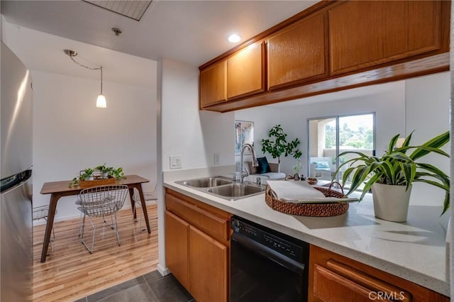 kitchen featuring dishwasher, a sink, freestanding refrigerator, brown cabinets, and decorative light fixtures