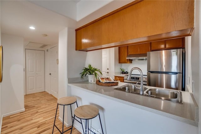 kitchen with appliances with stainless steel finishes, brown cabinets, under cabinet range hood, light wood-style floors, and a sink