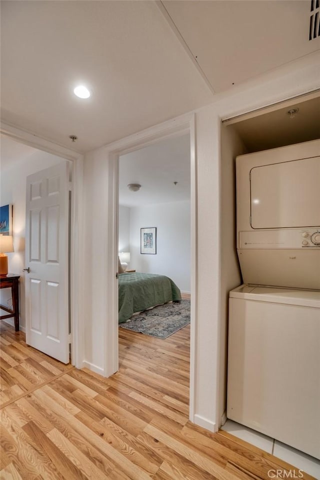 laundry area featuring stacked washing machine and dryer, light wood-style floors, and baseboards
