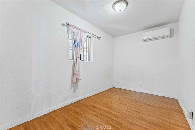 unfurnished room with a wall unit AC, wood finished floors, baseboards, and a textured ceiling