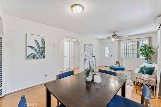 dining room with arched walkways, a ceiling fan, light wood finished floors, and a wall mounted air conditioner