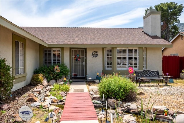 18993 Janisse Ln, Lake Elsinore, CA 92530 - view of exterior entry featuring stucco siding, a shingled roof, a chimney, and fence