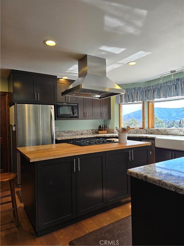1014 Dusty Rd, Frazier Park, CA 93225 - kitchen featuring island range hood, butcher block counters, black appliances, hardwood / wood-style flooring, and dark cabinets