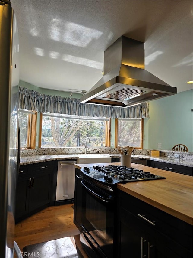 1014 Dusty Rd, Frazier Park, CA 93225 - kitchen with island range hood, appliances with stainless steel finishes, butcher block countertops, light wood finished floors, and dark cabinetry