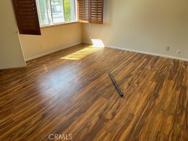 spare room with dark wood-type flooring and baseboards