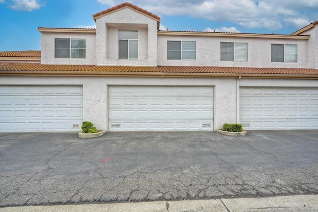 view of front facade with stucco siding, a tiled roof, driveway, and a garage