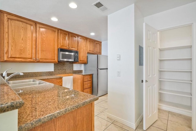 kitchen featuring freestanding refrigerator, a sink, light tile patterned floors, brown cabinets, and recessed lighting