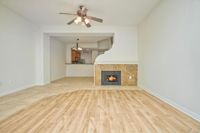 unfurnished living room with light wood-style floors, ceiling fan, a chandelier, a tile fireplace, and baseboards