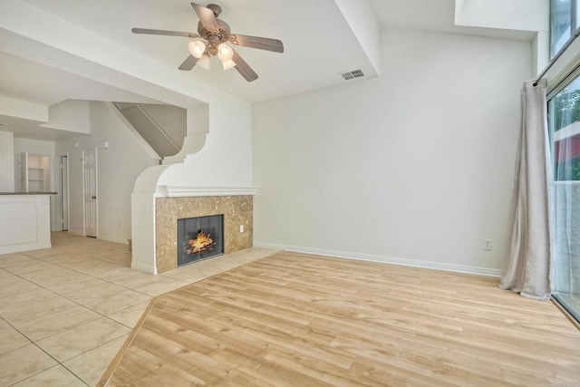 unfurnished living room with ceiling fan, a premium fireplace, light wood-style floors, and baseboards