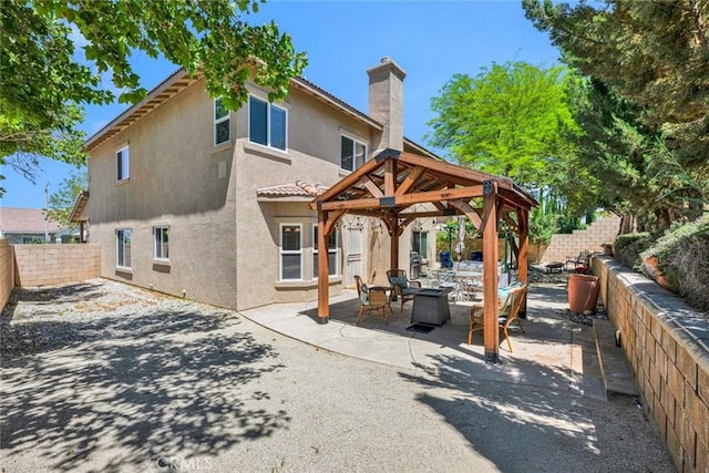 rear view of house featuring a gazebo, an outdoor fire pit, stucco siding, a patio area, and a chimney